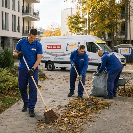 Trei hamali strâng cu mături frunzele căzute într-un sac mare, la curățare teritorii între blocuri