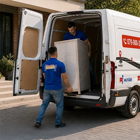 Hamalii fixează cu chingi canapeaua, scaunele și masa în dubă, la transport mobilă pentru birouri și afaceri